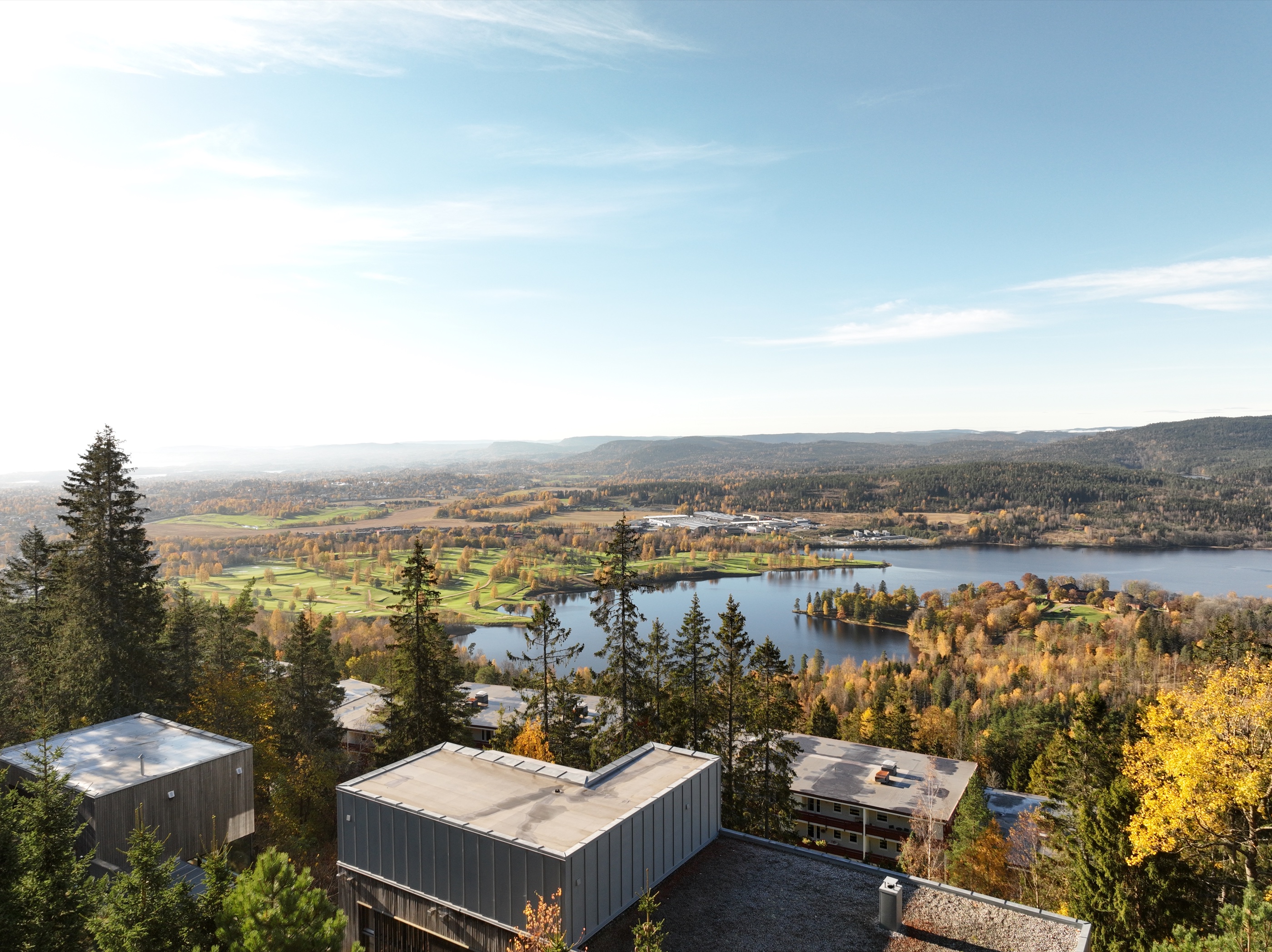 Åpent høstlandskap med vann, skog og bebyggelse fotografert fra luften